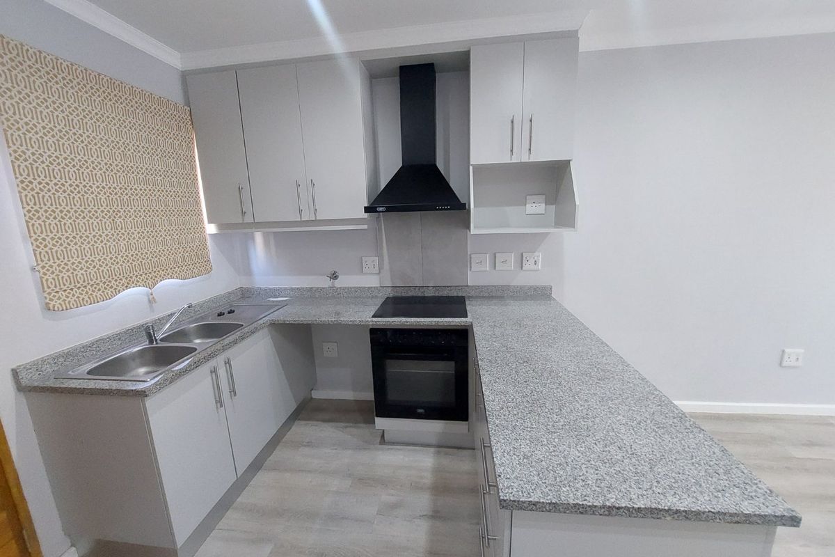 Modern kitchen featuring granite countertops, built-in oven, electric hob, extractor fan, and ample cabinetry, finished with light laminate flooring.