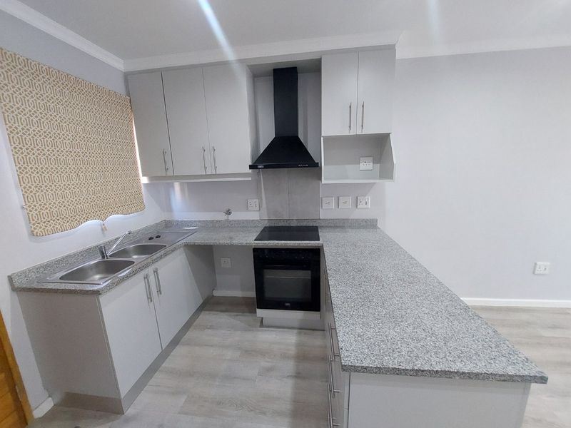 Modern kitchen featuring granite countertops, built-in oven, electric hob, extractor fan, and ample cabinetry, finished with light laminate flooring.