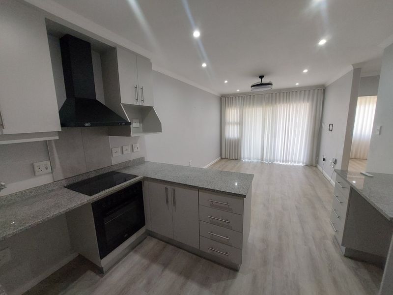 Modern open-plan kitchen and living area featuring granite countertops, built-in appliances, laminate flooring, and recessed lighting, offering a clean and versatile living space.