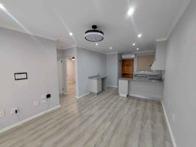 An open-plan living and kitchen area featuring modern laminate flooring, granite countertops, built-in cabinetry, and recessed lighting in a neutral color palette.