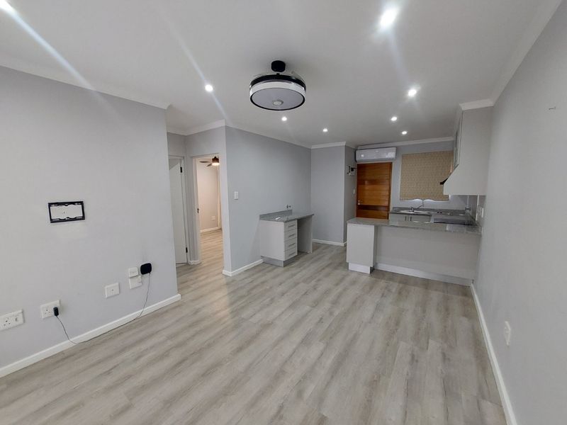 Modern open-plan living area featuring light laminate flooring, recessed lighting, and a functional kitchen with granite countertops and built-in cabinetry.
