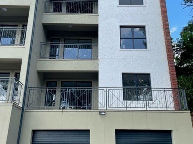 A modern multi-story apartment building facade featuring integrated garage doors, private balconies with metal railings, and clean architectural finishes.