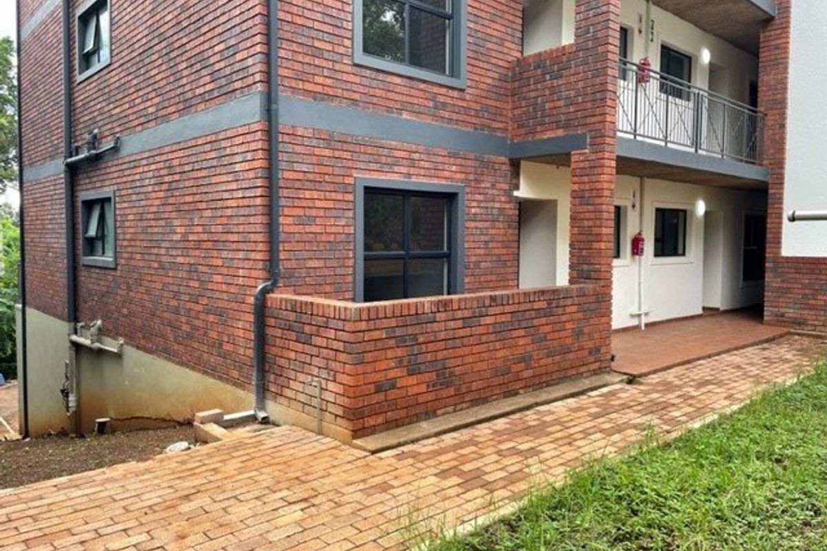 Exterior view of a multi-story apartment building featuring face brick facade, paved walkways, and balcony access with metal railings.
