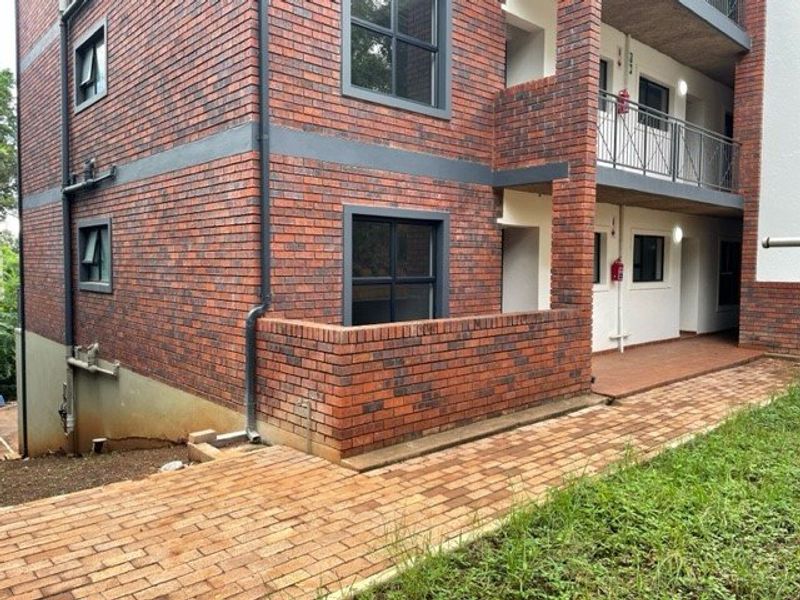 Exterior view of a multi-story apartment building featuring face brick facade, paved walkways, and balcony access with metal railings.