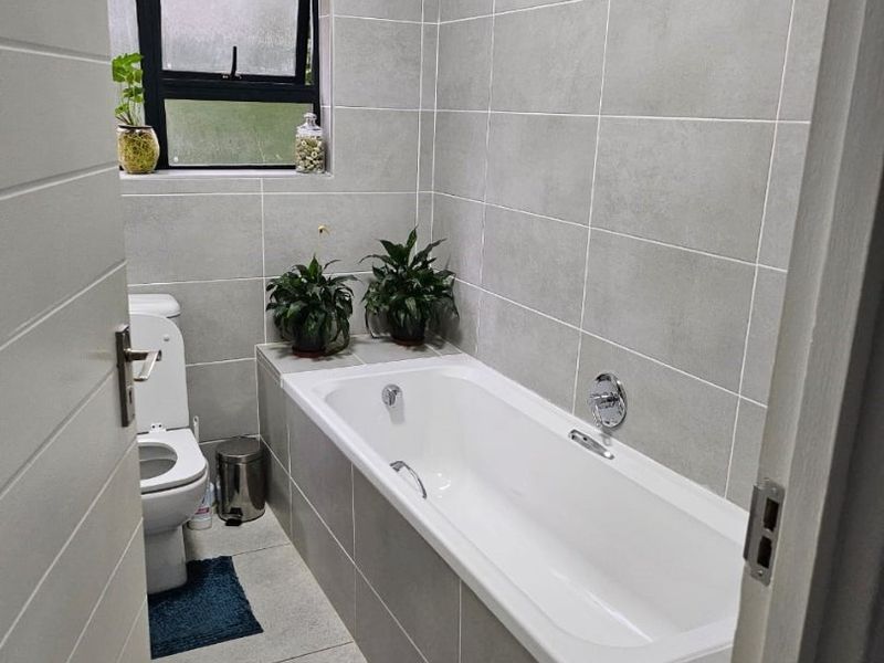 A modern bathroom featuring a built-in bathtub, tiled walls and flooring, and a top-hung window for natural light.