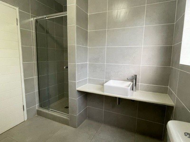 A modern bathroom featuring a glass-enclosed shower, a minimalist vessel sink on a floating vanity shelf, and neutral floor-to-ceiling ceramic tiling.
