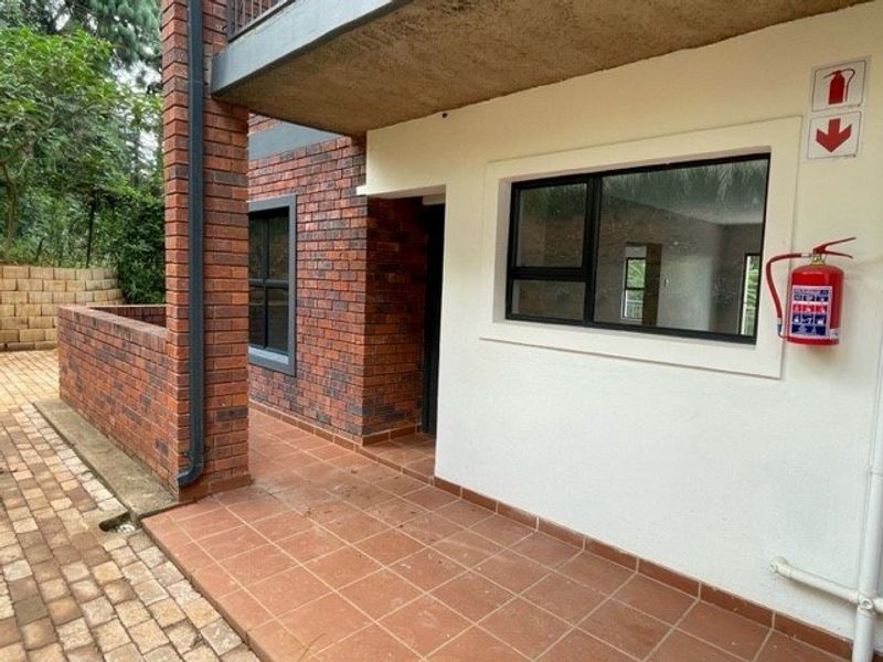 Exterior view of an apartment entrance featuring a brick facade, tiled patio area, and installed fire safety equipment.