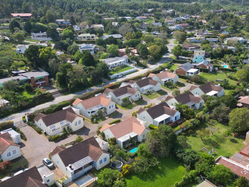 An aerial view of a residential estate featuring multiple detached houses with tiled roofs, paved driveways, and established garden areas.