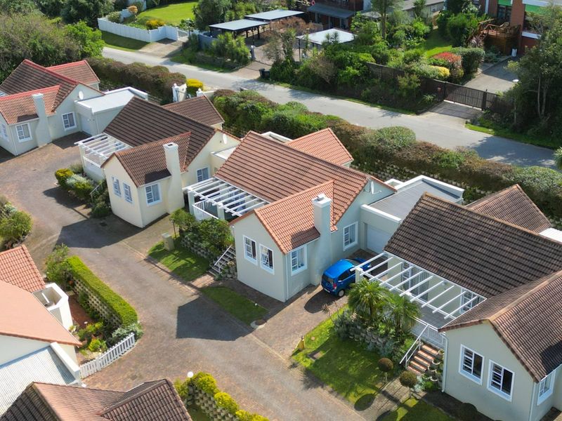 An aerial view of a residential complex featuring multiple houses with tiled roofs, paved driveways, and private garden spaces.