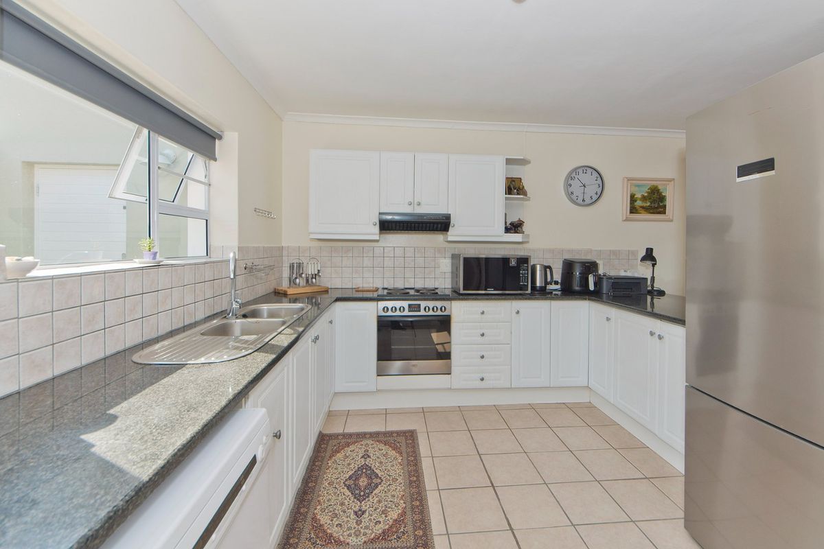 A functional kitchen featuring white cabinetry, granite countertops, a built-in oven with hob, and tiled flooring, offering a clean and practical workspace.
