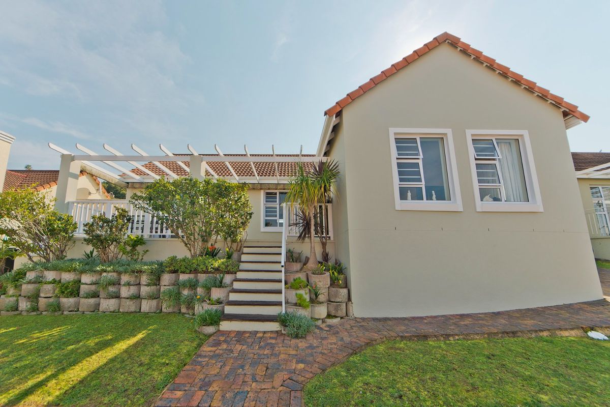 Rear view of the property featuring a raised terrace with a pergola, brick paved pathway, and landscaped retaining walls.