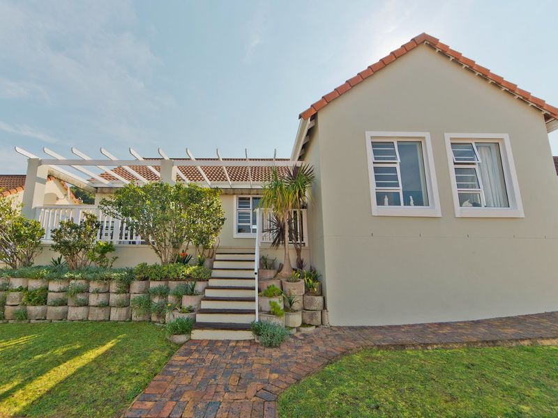 Rear view of the property featuring a raised terrace with a pergola, brick paved pathway, and landscaped retaining walls.