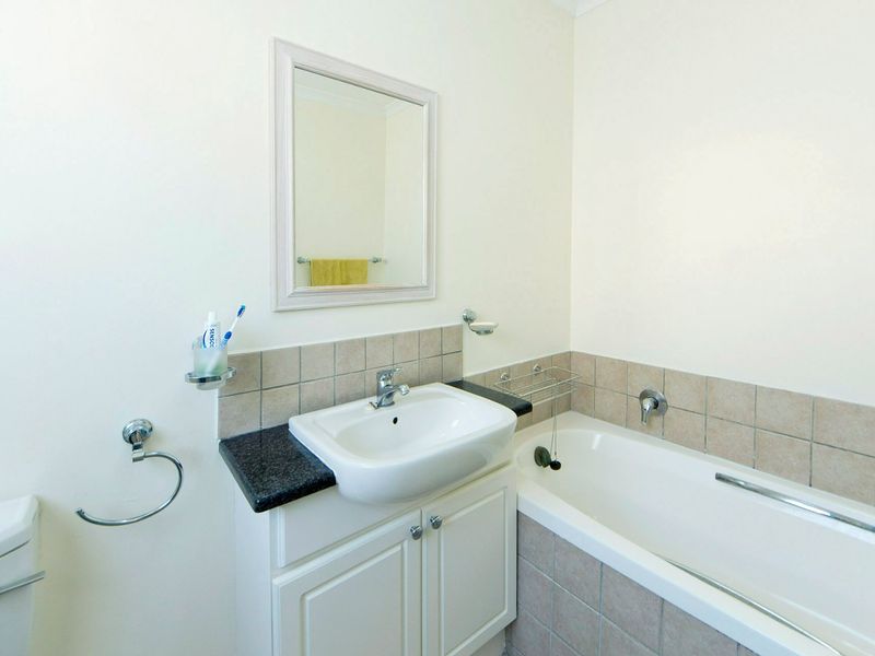 A clean and functional bathroom featuring a vanity with basin, bathtub with tiled surround, and a wall-mounted mirror.