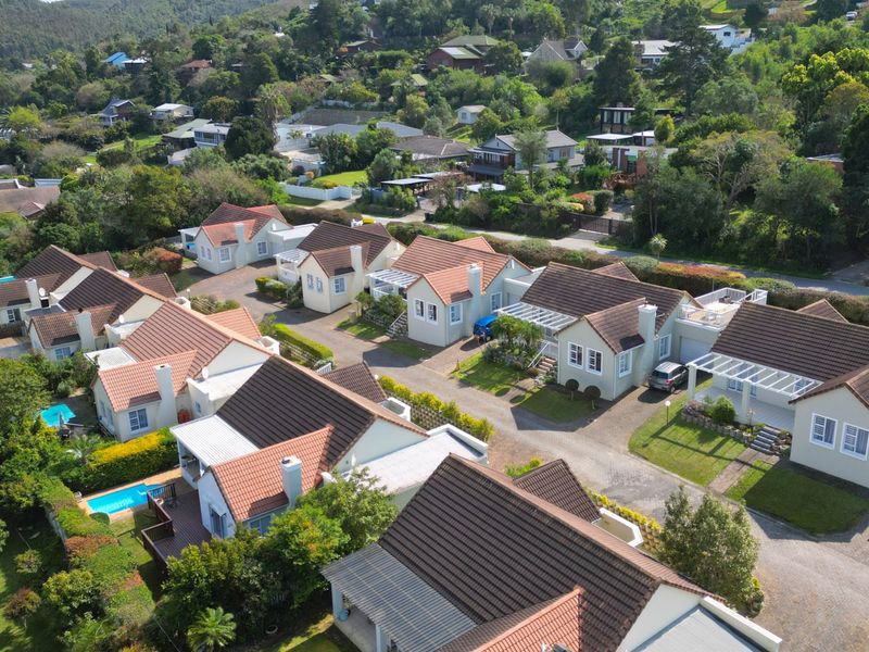 An aerial view of a residential estate featuring multiple detached houses with tiled roofs, paved driveways, and landscaped gardens.