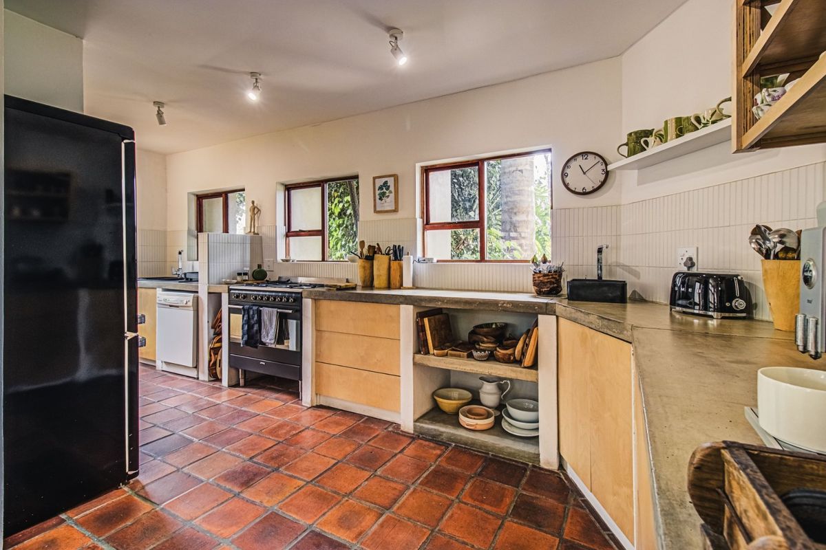 A well-lit kitchen featuring concrete countertops, timber cabinetry, a gas hob, and terracotta tiled flooring with a clean subway tile backsplash.