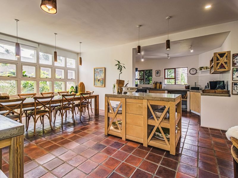 Spacious open-plan kitchen and dining area featuring terracotta floor tiles, a central kitchen island, and large windows providing natural light.