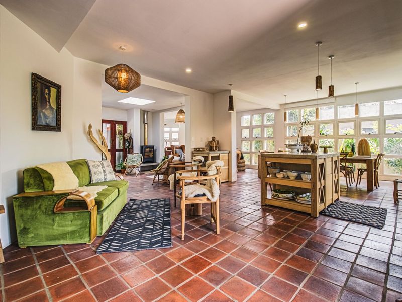 Spacious open-plan living area featuring terracotta floor tiles, a wood-burning fireplace, abundant natural light from large multi-pane windows, and a skylight.