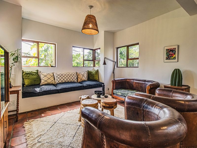 A cozy living room featuring terracotta tile flooring, a built-in window seat, and large casement windows overlooking the garden.