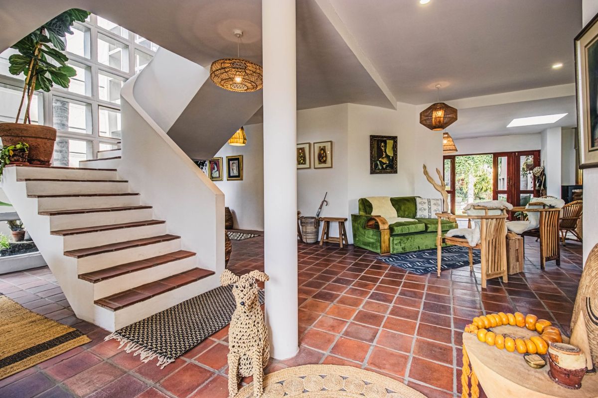 Spacious living area featuring classic terracotta tile flooring, a striking curved staircase, and a central structural column with natural light from a skylight.