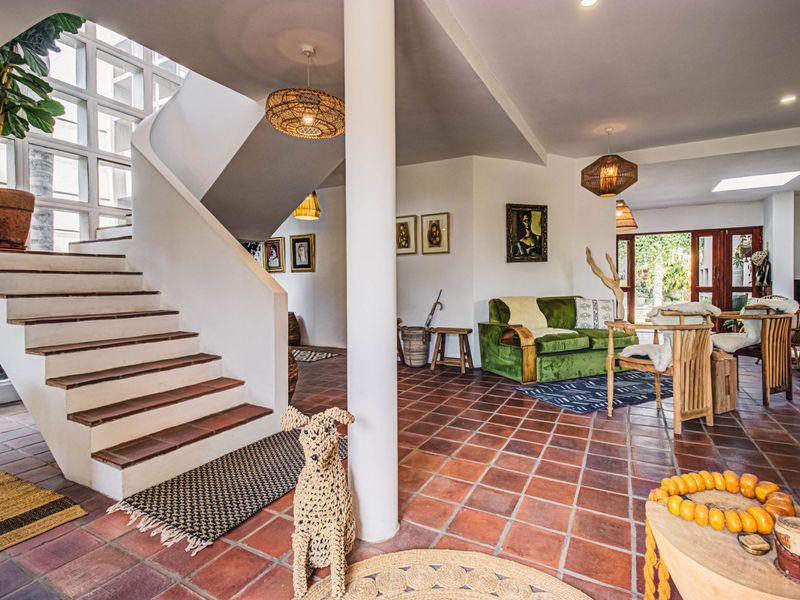Spacious living area featuring classic terracotta tile flooring, a striking curved staircase, and a central structural column with natural light from a skylight.