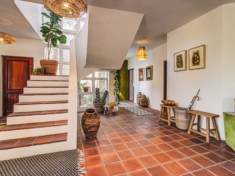 Spacious entrance hall featuring terracotta tile flooring, a prominent staircase, and natural light through multi-pane windows.
