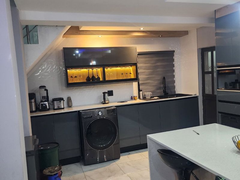 Modern kitchen featuring sleek dark cabinetry, stone countertops, integrated sink, under-cabinet lighting, and a functional kitchen island with tiled flooring.