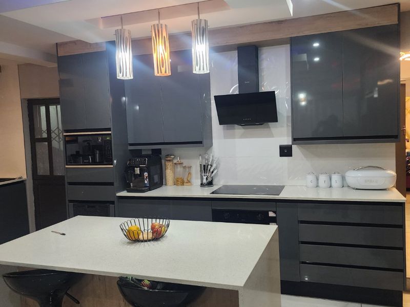 Modern kitchen featuring high-gloss cabinetry, a central island with quartz countertops, integrated appliances, and stylish recessed ceiling lighting with blue accent features.