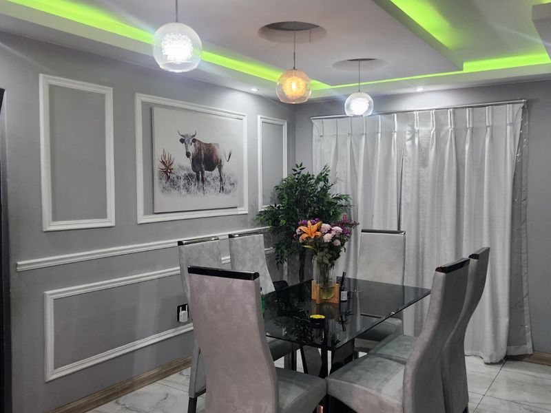 A modern dining room featuring decorative wainscoting, marble-look floor tiles, and a sophisticated recessed ceiling with integrated green LED accent lighting.