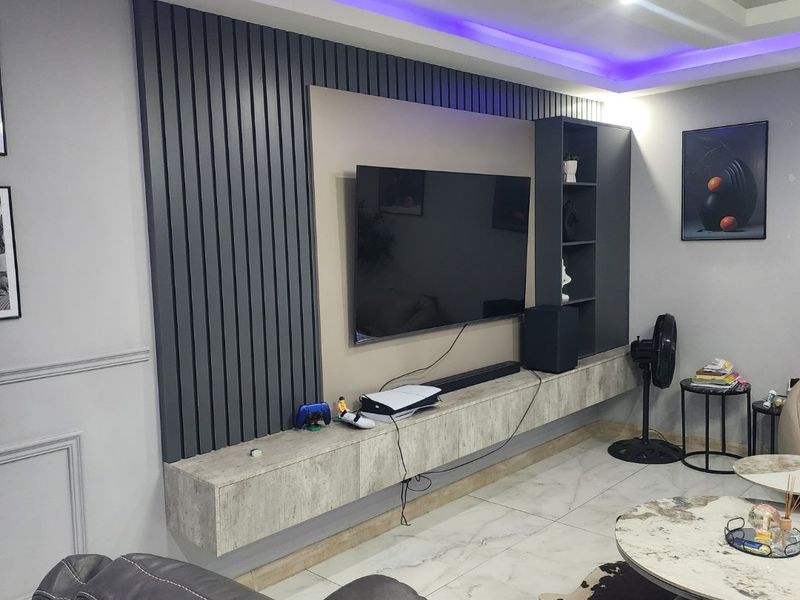 Modern living room featuring a custom slatted feature wall, floating media console, built-in shelving, and ambient LED ceiling lighting.