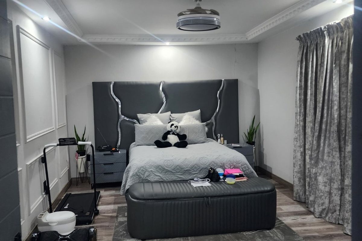 A bedroom featuring crown molding, wainscoting, and laminate flooring, with a visible crack in the wall finish above the headboard area.