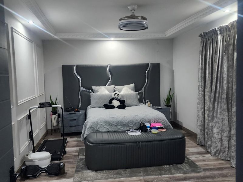 A bedroom featuring crown molding, wainscoting, and laminate flooring, with a visible crack in the wall finish above the headboard area.