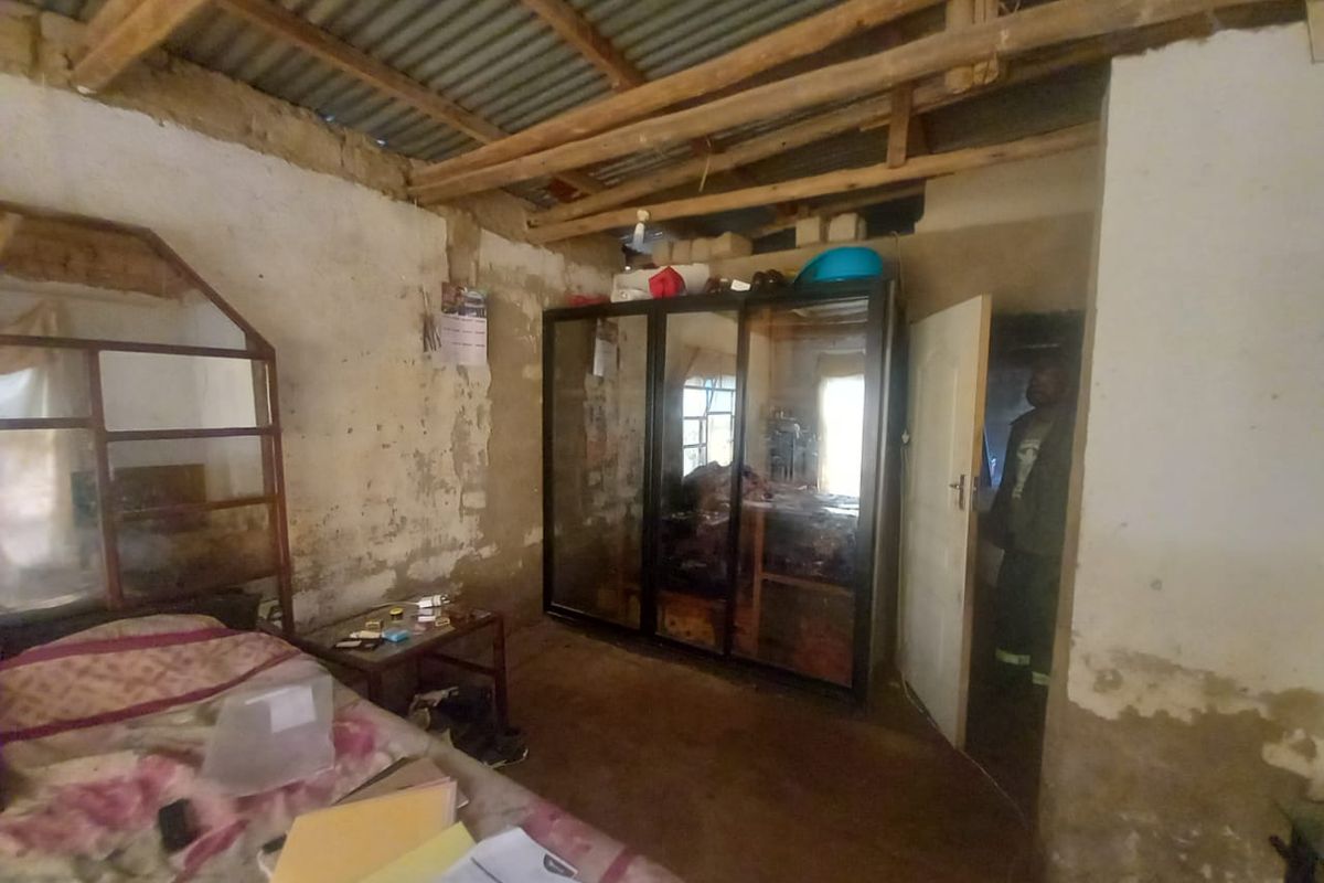 A bedroom featuring exposed timber rafters and corrugated metal roofing, requiring significant renovation to address wall plaster deterioration and overall structural finish.