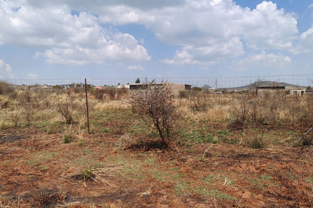 A view of a vacant residential plot featuring dry natural vegetation and perimeter wire mesh fencing.