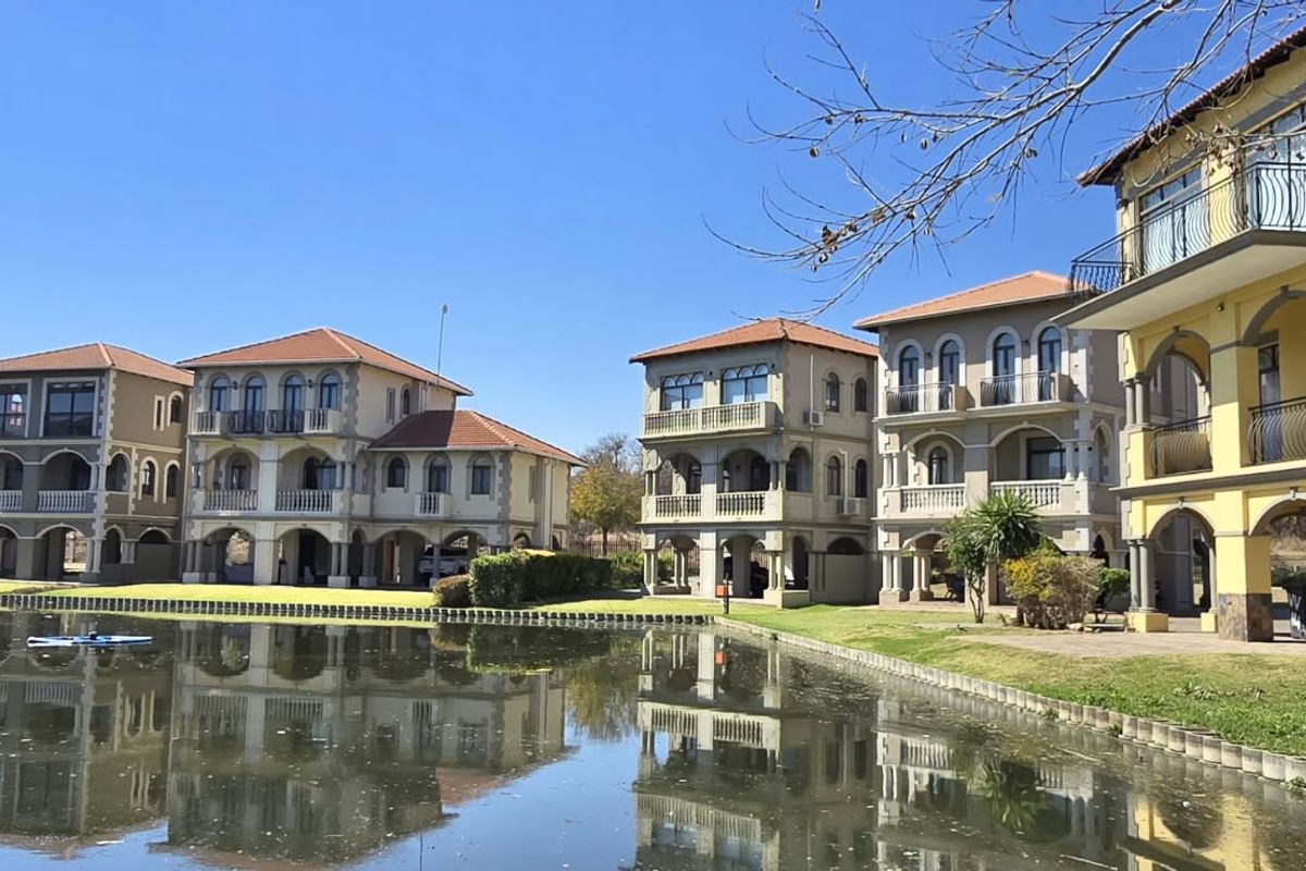 A scenic view of multi-story residential villas featuring Mediterranean-style architecture, arched balconies, and tiled roofs, situated directly along a waterfront.