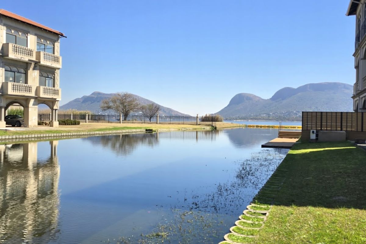 Scenic view of a canal-front property featuring a private jetty, manicured lawns, and mountain vistas in the background.