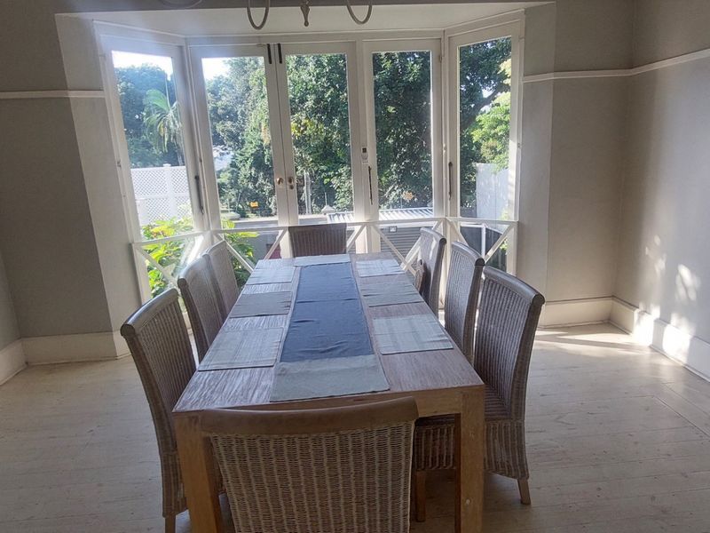 A bright dining room featuring timber flooring, classic picture rails, and a large bay window with French doors opening to the garden.