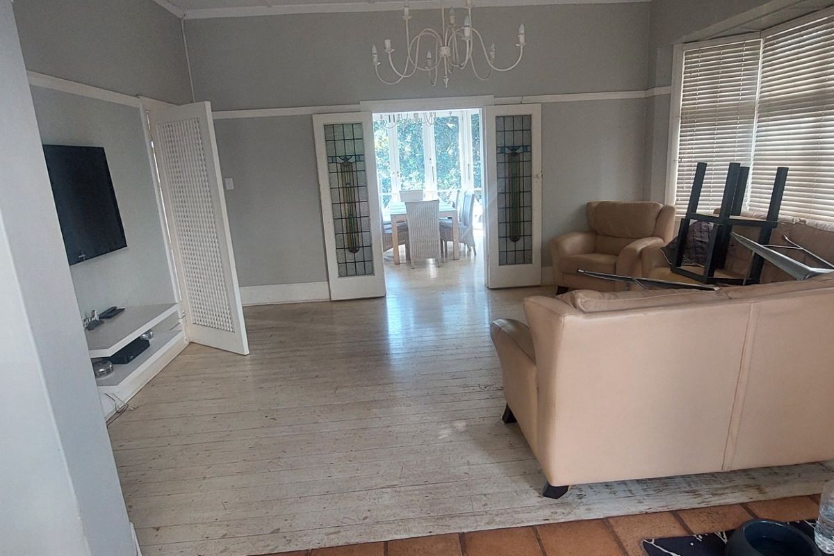 Spacious living room featuring original hardwood flooring, classic leaded glass double doors, and built-in shelving, offering a bright and character-filled living space.