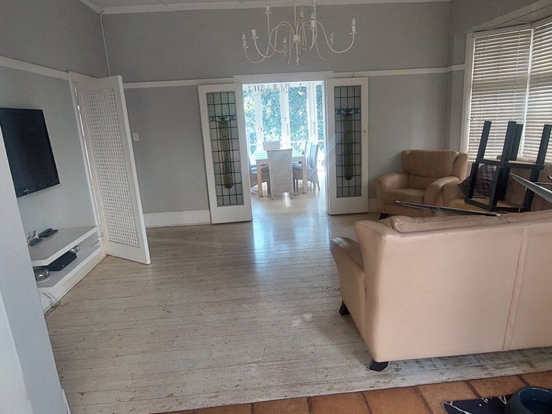 Spacious living room featuring original hardwood flooring, classic leaded glass double doors, and built-in shelving, offering a bright and character-filled living space.