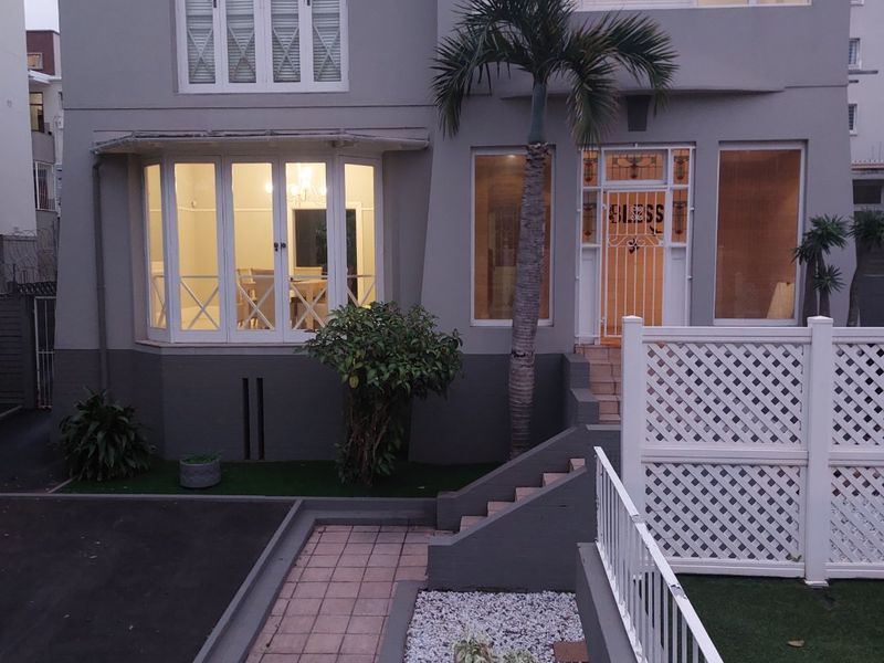 Front elevation of a two-story house featuring a tiled roof, bay window, security entrance gate, paved walkway, and landscaped garden area.