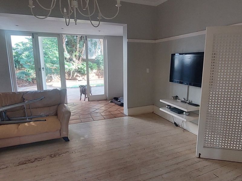 Spacious living room featuring original hardwood flooring, built-in shelving, and sliding glass doors that open onto a tiled patio area.
