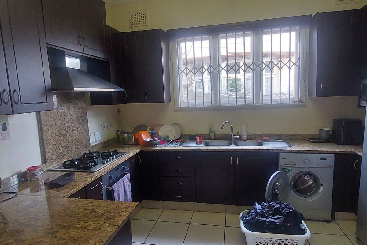 Functional kitchen featuring dark wood cabinetry, granite countertops, a gas hob, extractor fan, and integrated laundry space with tiled flooring.