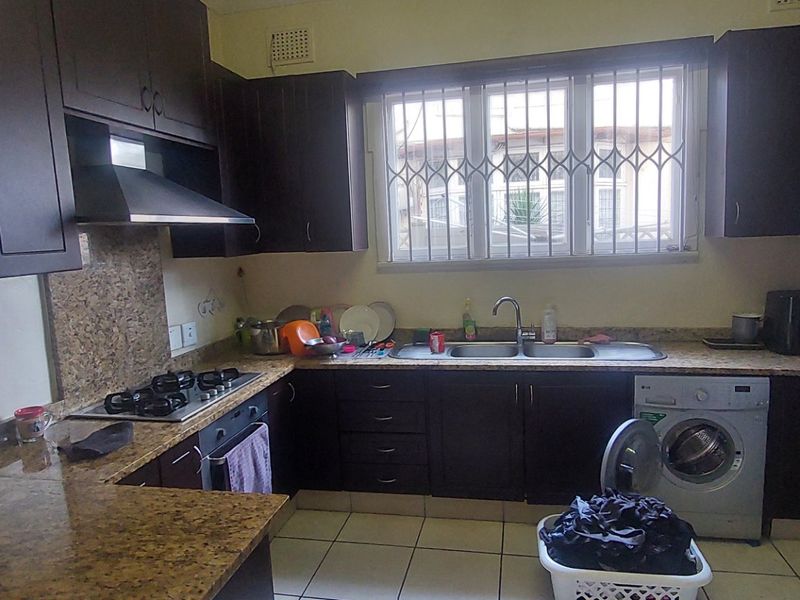 Functional kitchen featuring dark wood cabinetry, granite countertops, a gas hob, extractor fan, and integrated laundry space with tiled flooring.