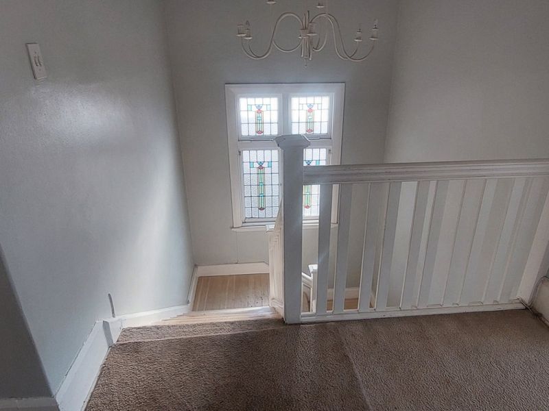 A bright landing area featuring a classic wooden balustrade, a decorative stained glass window, and a traditional chandelier above the staircase.