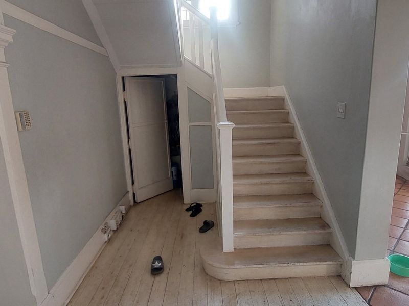 Entrance hall featuring a wooden staircase with under-stair storage, transitioning from light wood flooring to terracotta tiles near the exterior door.