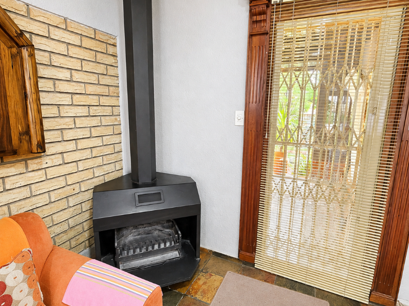 Living room featuring a corner fireplace, exposed brick wall, slate tile flooring, and a wooden door frame leading to an outdoor area.