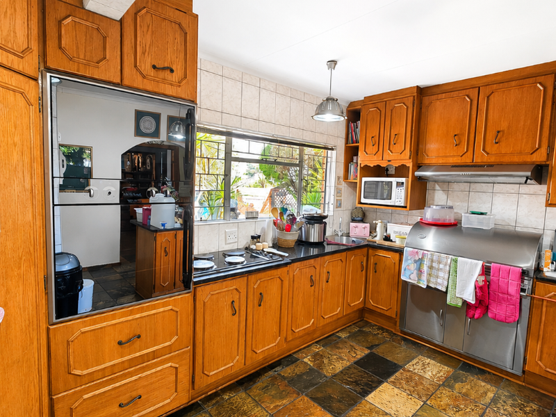 A functional kitchen featuring traditional wooden cabinetry, black granite countertops, stainless steel appliances, and distinctive slate tile flooring.