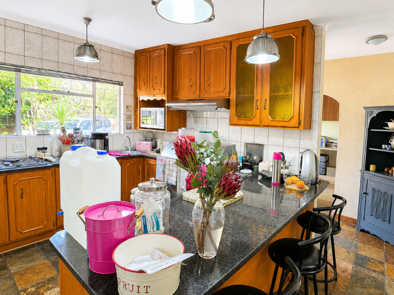 A functional kitchen featuring wooden cabinetry, granite countertops, a built-in extractor fan, and tiled flooring with a central breakfast bar island.
