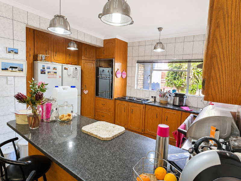 A functional kitchen featuring wooden cabinetry, granite countertops, a built-in oven, and a breakfast bar with pendant lighting.