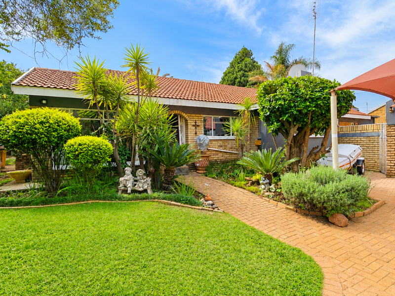 A well-maintained single-story brick house featuring a tiled roof, a neat front lawn, and a paved walkway leading to the entrance.