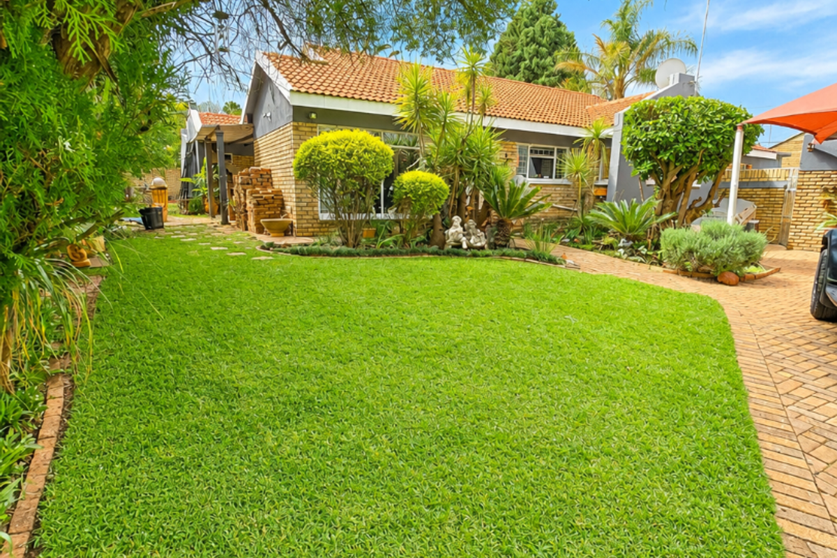 A well-maintained rear garden featuring a lush green lawn, established landscaping, and brick-paved pathways leading to the rear facade of the house.